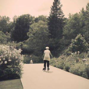 older adult skating on a path through a park, with trees and flowers in the background. The image is in black and white, with a vintage feel. The mood is peaceful and calming, and the aesthetic is serene and natural.