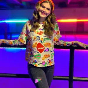 a medium shot of a cheerful, young adult at a roller skating rink wearing a bright and colorful outfit. The mood should be light and fun, with the skater smiling and enjoying the moment. The aesthetic should be modern and vibrant, with bright colors and patterns that stand out against the dark background of the rink.